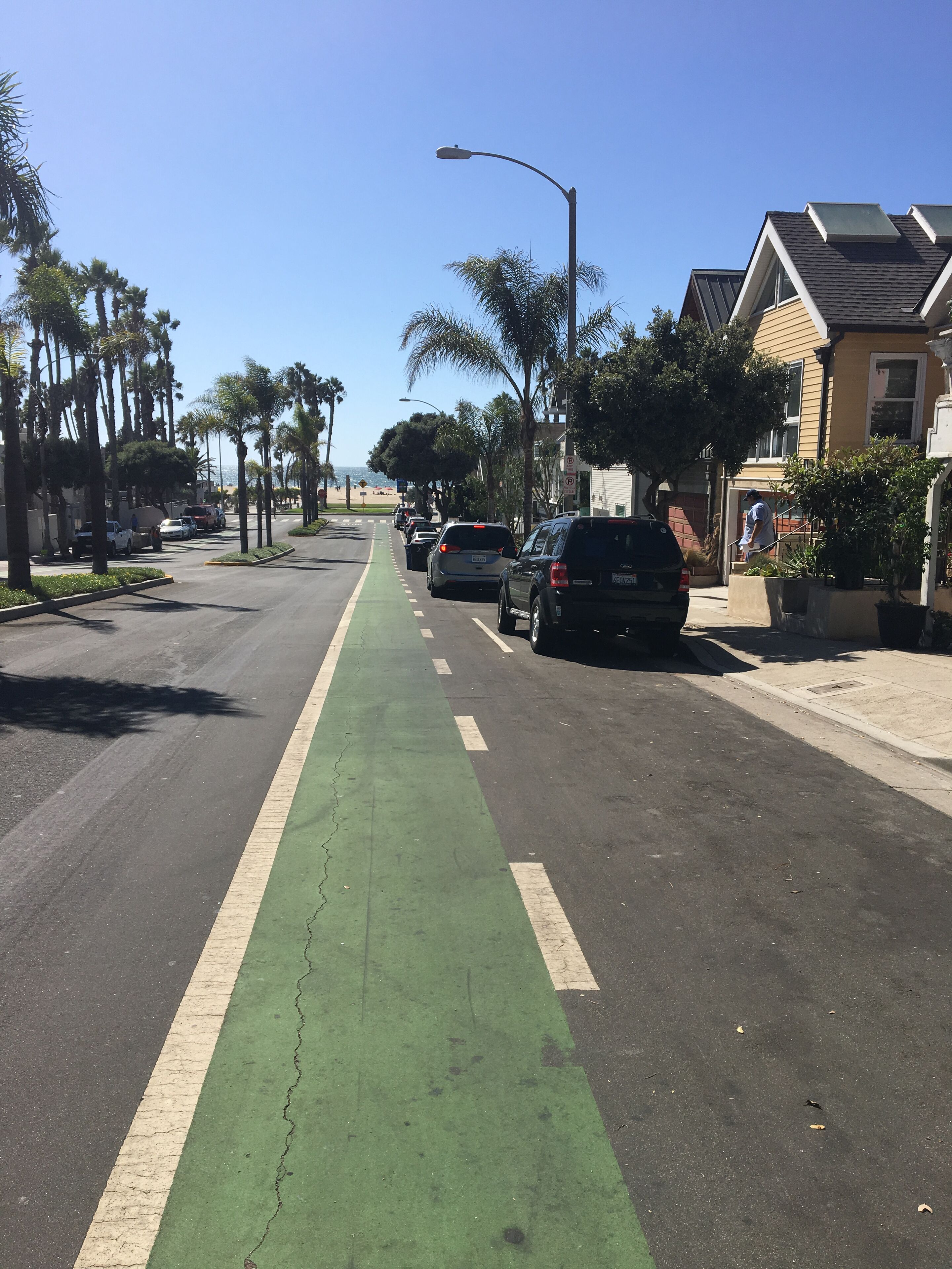 A street with a green bike lane, parked cars, and residential buildings.