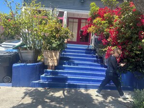 Une personne qui passe devant un bâtiment avec des marches bleues et des plantes en pot.