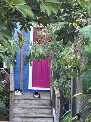 A wooden staircase leading to a door with a blue and pink facade, surrounded by greenery. - Santa Monica  Garden Beach Bungalow     Private, Quiet, and Steps from the Sand (Santa Monica)