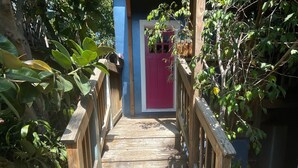 A wooden staircase leading to a building with a red door, surrounded by greenery.