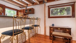 A room with a wooden ceiling, a desk with drawers, a bench, and a window with a view of trees.
