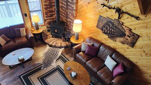 Un salon chaleureux avec des canapés en cuir, une table basse ronde, un tapis à motifs zébrés et un poêle à bois.
