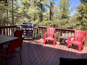 Eine Holzterrasse mit Grill, roten Adirondack-Stühlen und einem Tisch.