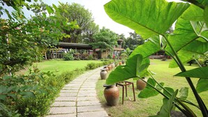 A stone pathway leading through a lush garden with large potted plants and a wooden structure in the background. - Lohas Gallery Long Stay Hostel (New Taipei City)