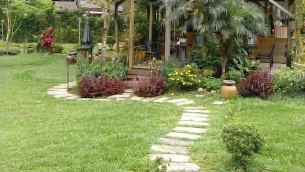 A two-story wooden structure with a covered porch, surrounded by lush greenery and a stone pathway. - Lohas Gallery Long Stay Hostel (New Taipei City)