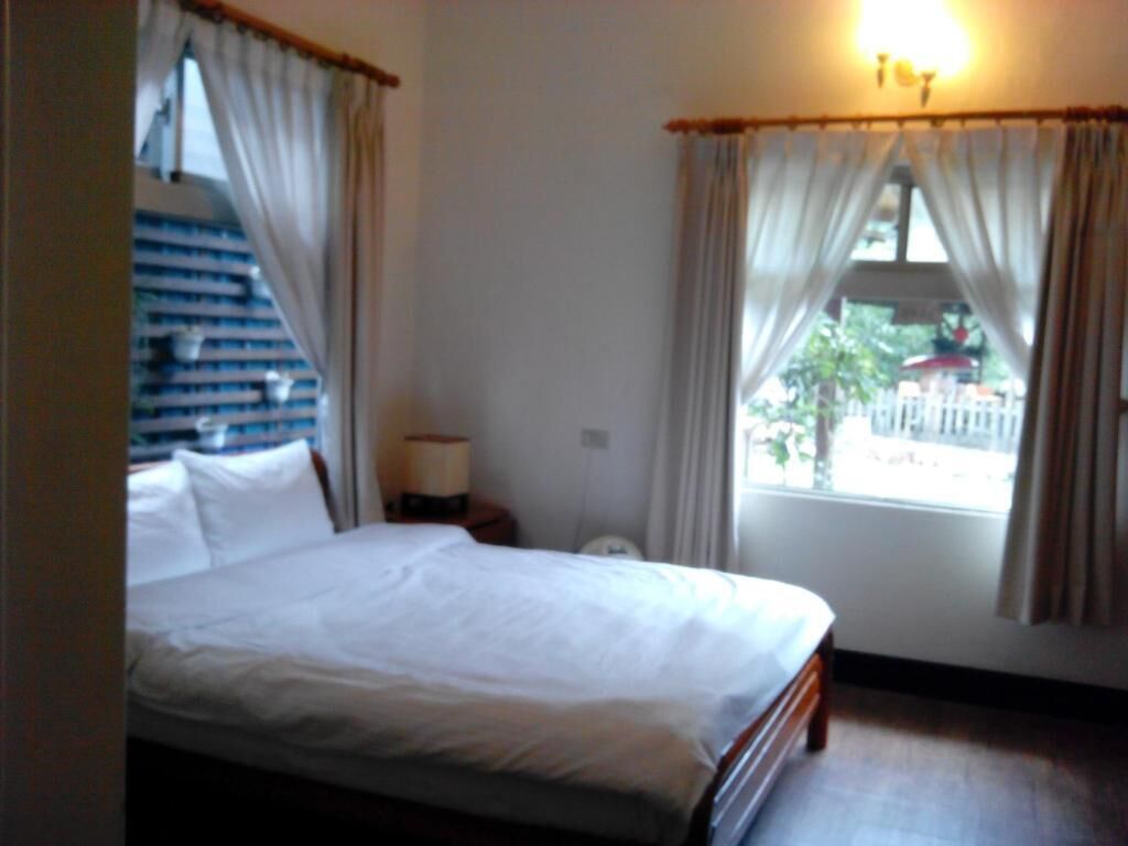 A bedroom with a bed, a nightstand, a lamp, and a window with curtains.