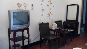 A hotel room with a television on a wooden stand, a small table with a kettle and cup, two chairs, and a mirror on the wall. - Lohas Gallery Long Stay Hostel (New Taipei City)