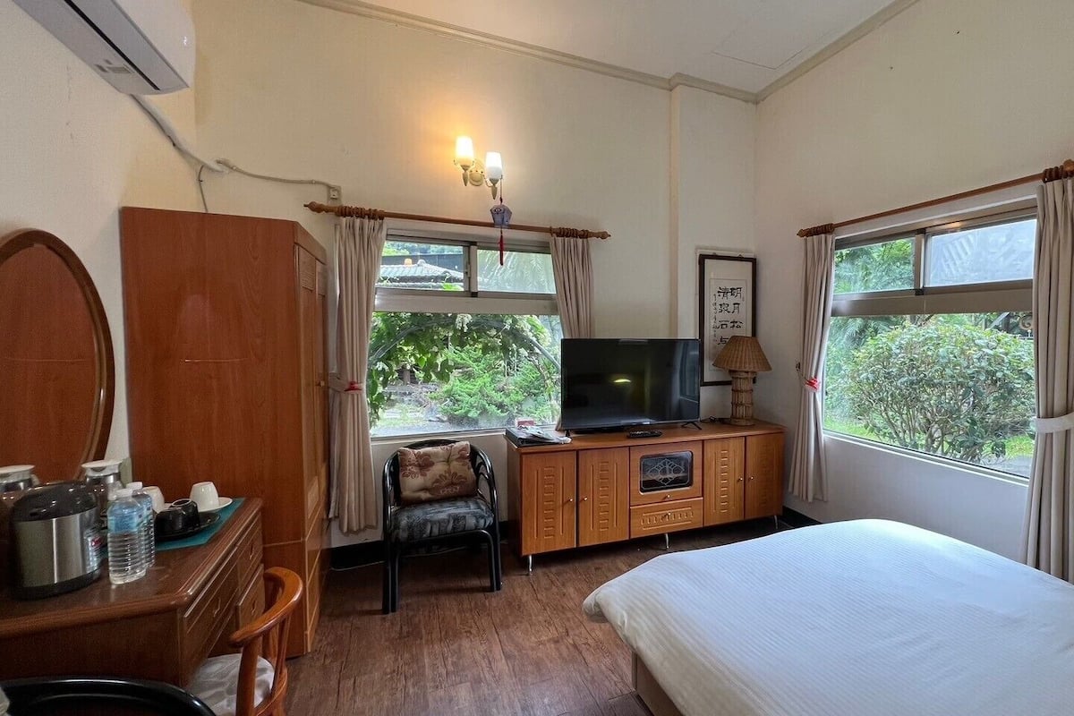 A hotel room with a bed, a TV, a desk with a lamp, a chair, and a wardrobe.