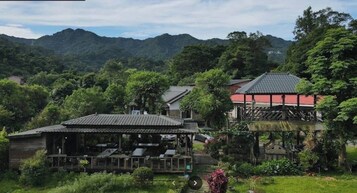 A traditional Japanese ryokan with a wooden deck, a red building, and a mountainous backdrop.