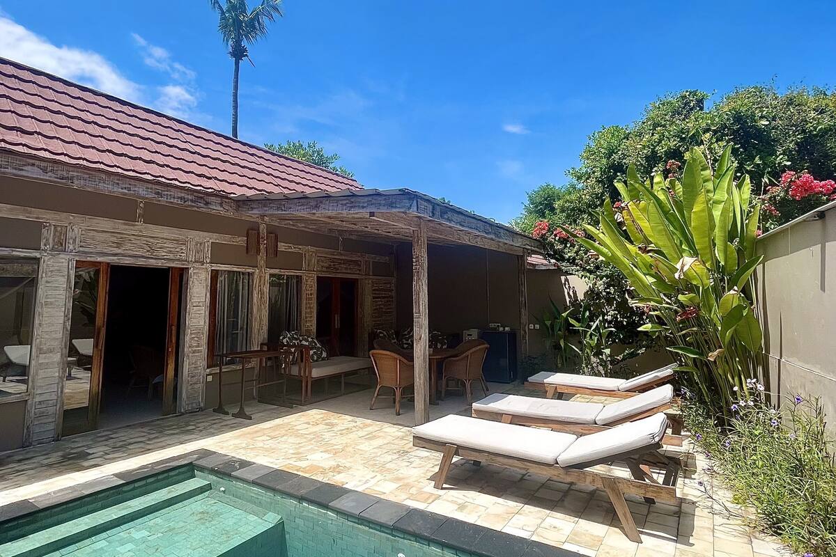 A poolside area with lounge chairs, a covered patio, and a building with a red roof.