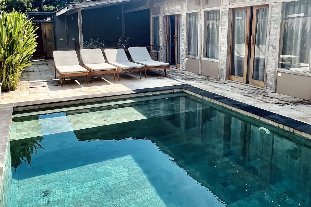 A swimming pool with clear water, two lounge chairs, and a covered patio area.