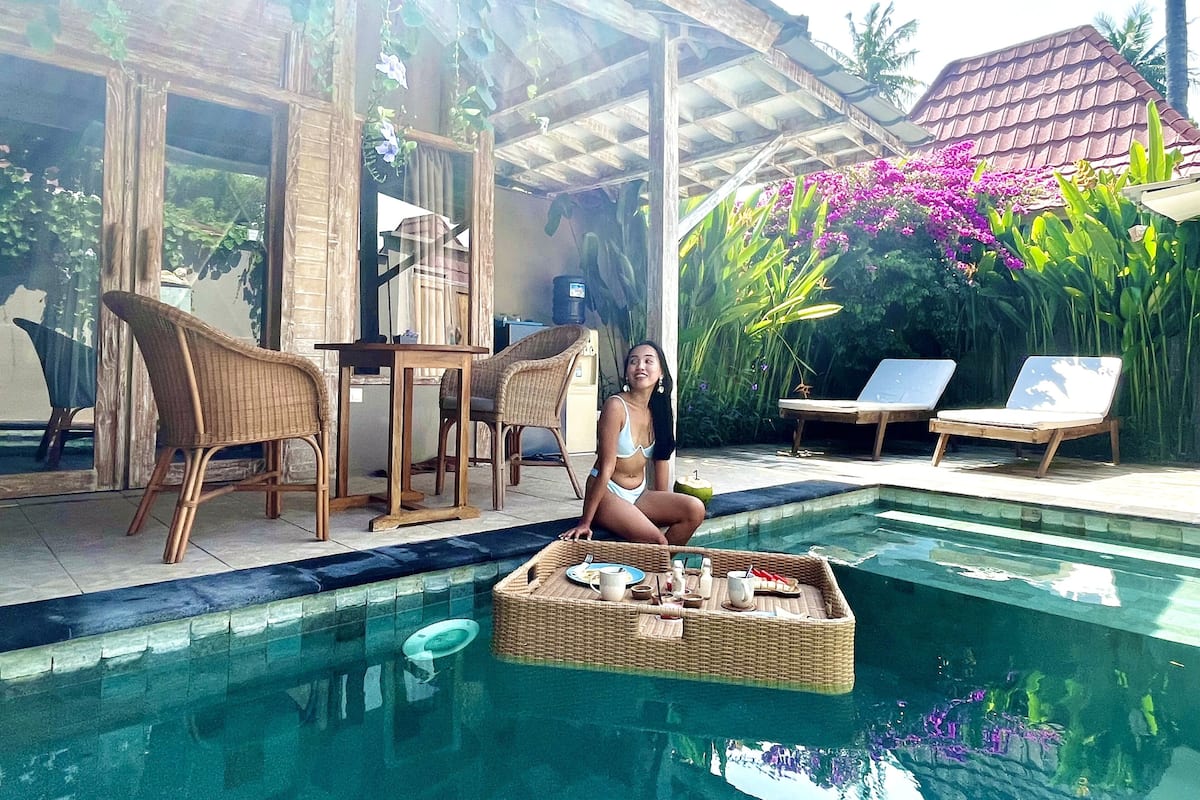 A poolside area with wicker furniture, a dining setup, and lush greenery.