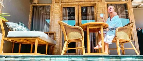 A poolside area with wicker furniture, a glass-enclosed room, and a view of the pool.
