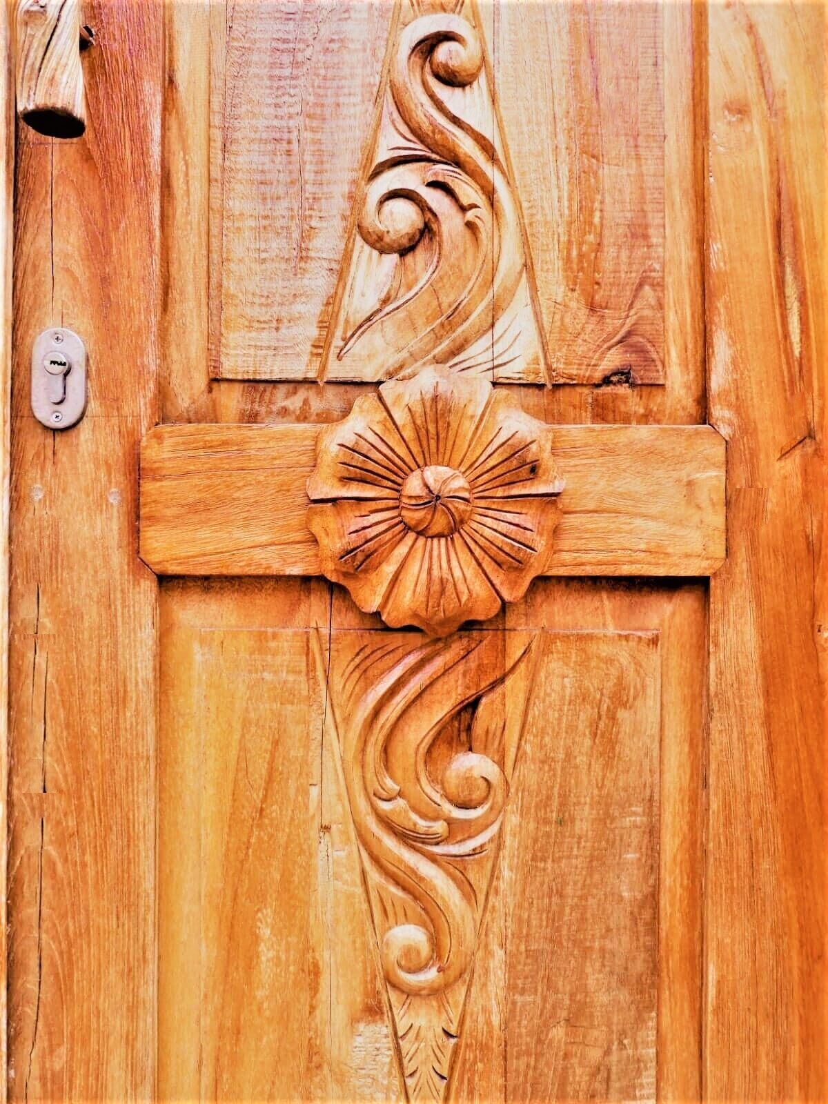 Une porte en bois ornée de sculptures complexes, notamment un motif floral central et des motifs enroulés.