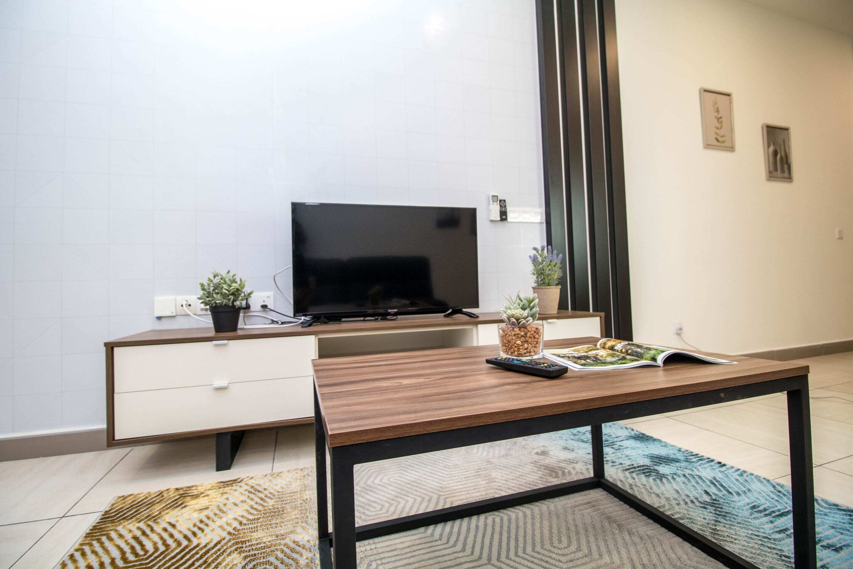 A modern living room with a flat-screen TV, wooden coffee table, and two potted plants.