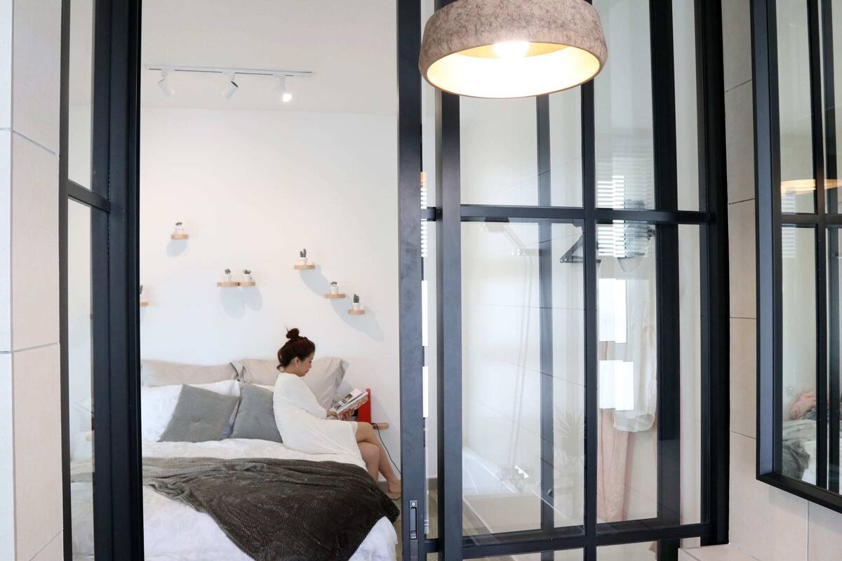Quarto moderno com cama, abajur e uma janela grande.