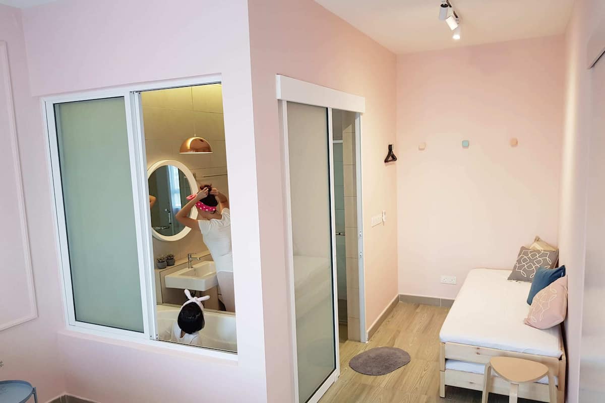 Quarto moderno com porta deslizante para um banheiro, uma cama com almofadas e uma pequena cadeira de madeira.