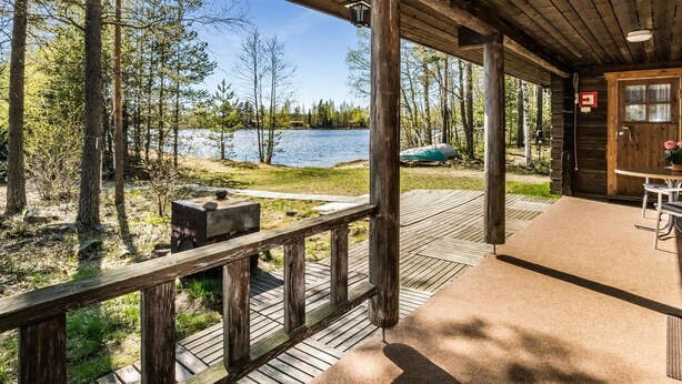 A wooden deck with a view of a lake, a grill, and a table with chairs. - Kesäranta 7 by Interhome (Kesälahti)