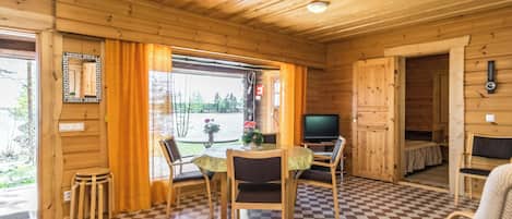 L’intérieur d’un chalet en bois comprend un coin repas, un téléviseur et un sol à carreaux.