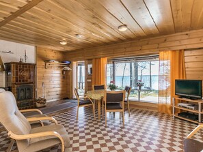 Ein Urlaubsdomizil mit Schachbrettmuster-Boden, Holzwänden, Kamin, Fernseher und Blick ins Freie.