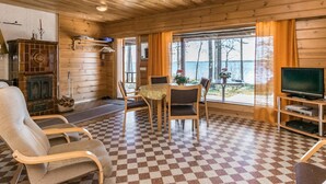 A cozy cabin interior with a checkered floor, wooden walls, a fireplace, a dining area with chairs and a table, and a TV on a stand. - Kesäranta 7 by Interhome (Kesälahti)