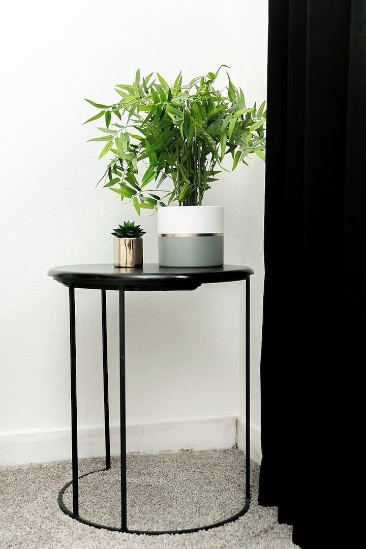 A small round table with a potted plant and a small decorative item on it, against a plain wall.