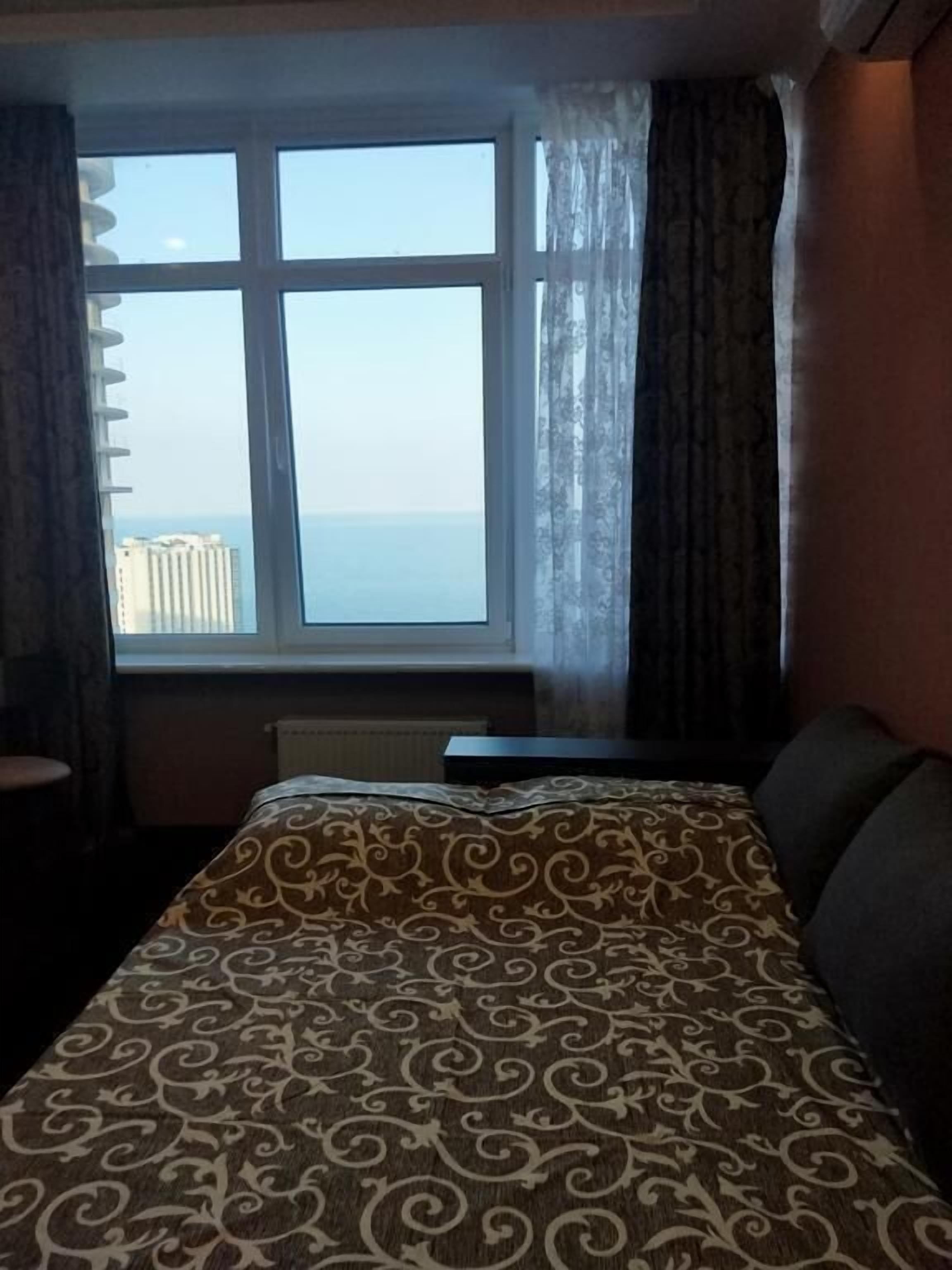 Habitación de hotel con una cama grande, vista al mar y una ventana con cortinas.
