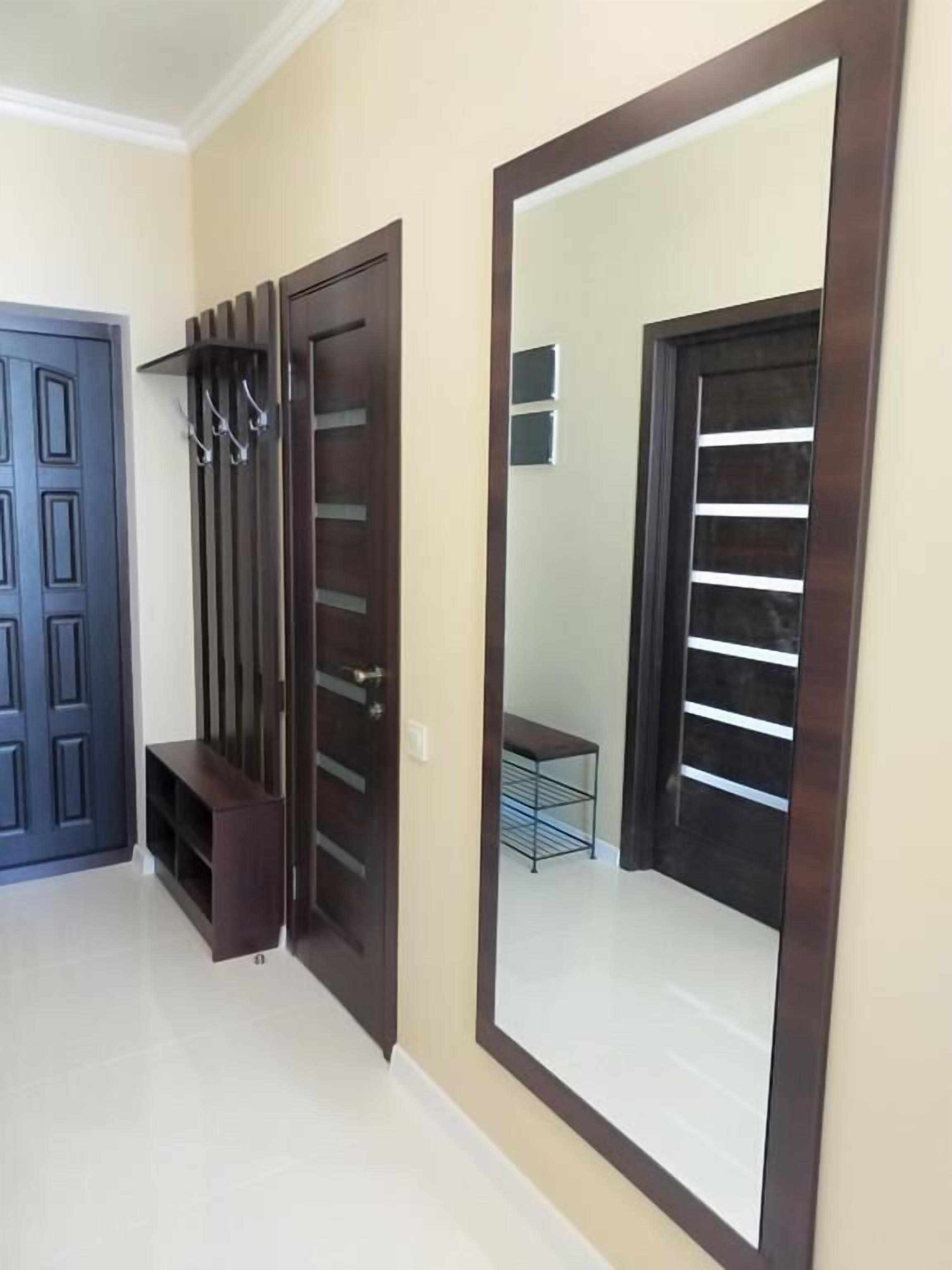 A hallway with a large mirror, a dark wooden door with a bench, and a metal rack.