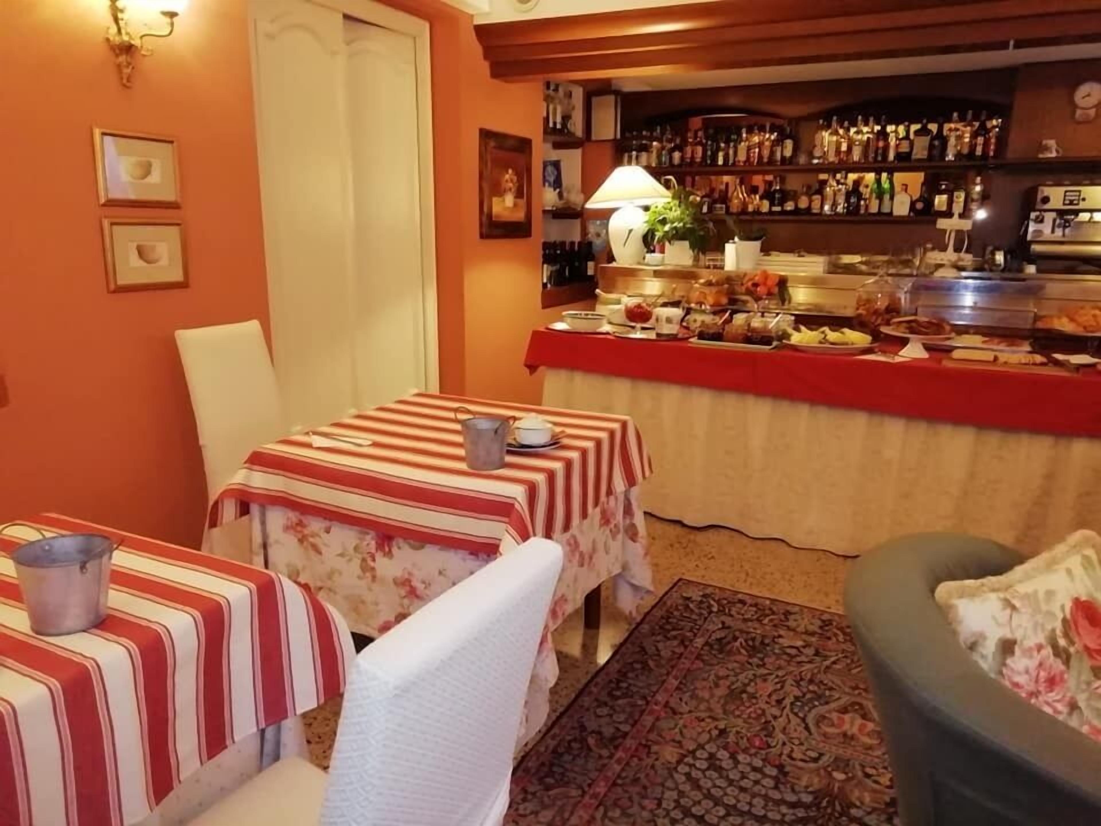 Ein Essbereich mit gestreiften Tischdecken, eine Bar mit verschiedenen Flaschen und ein Teppich mit floralem Muster.
