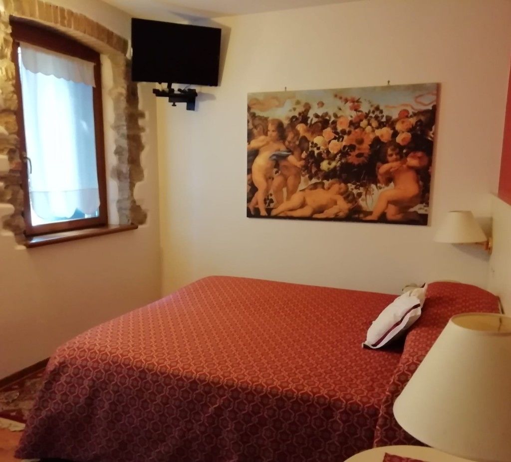 Une chambre à coucher avec un lit, un tableau, une télévision et une fenêtre avec des rideaux.