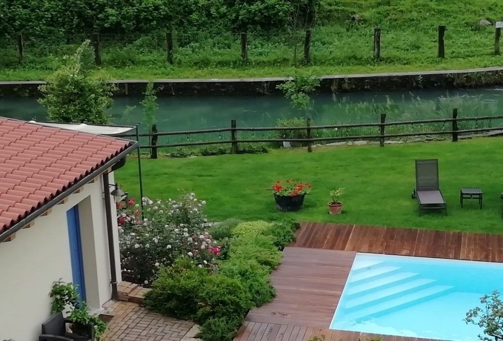 Un patio trasero con piscina, terraza de madera y vista al río.