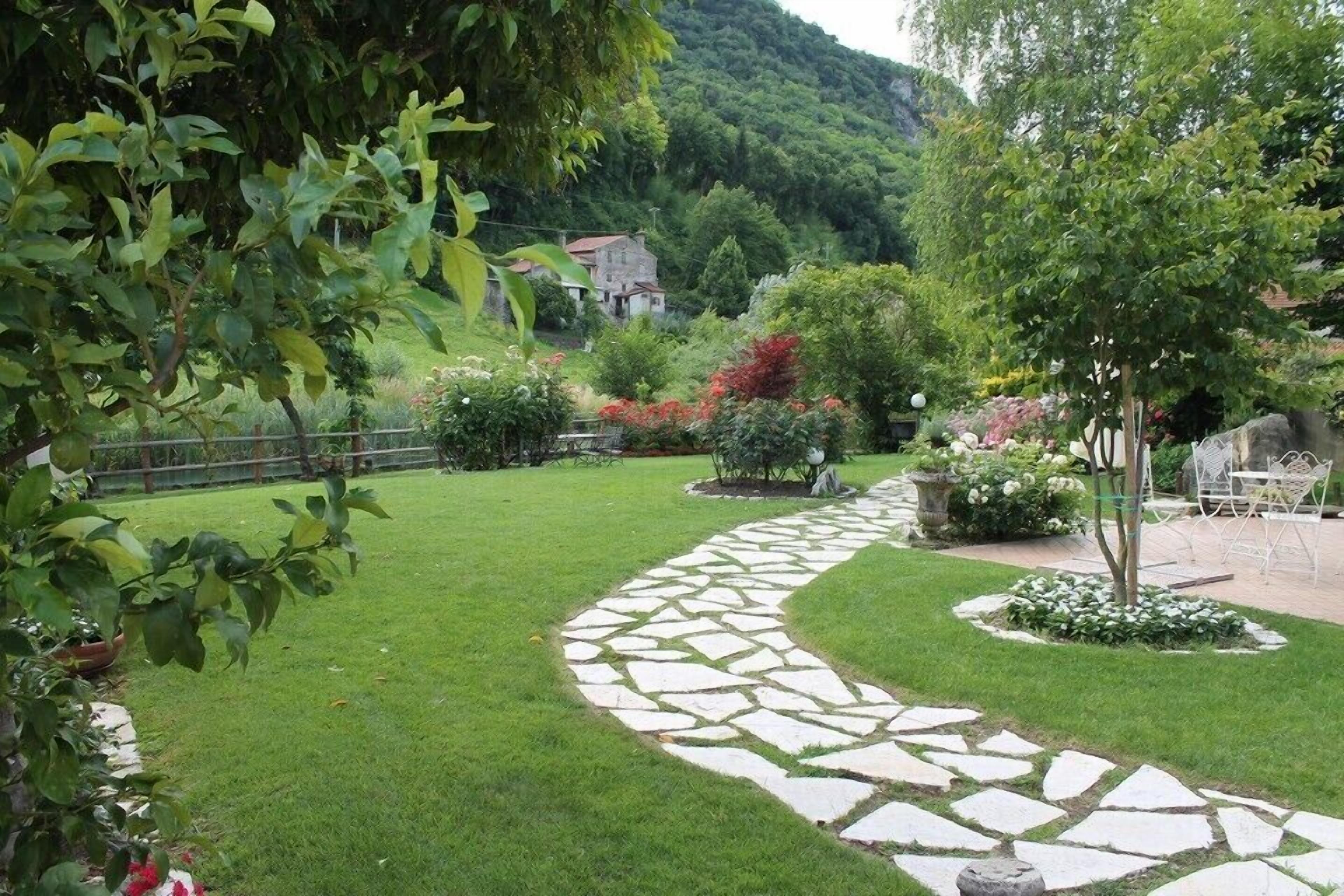 A stone pathway winding through a well-maintained garden with lush greenery and a variety of plants.
