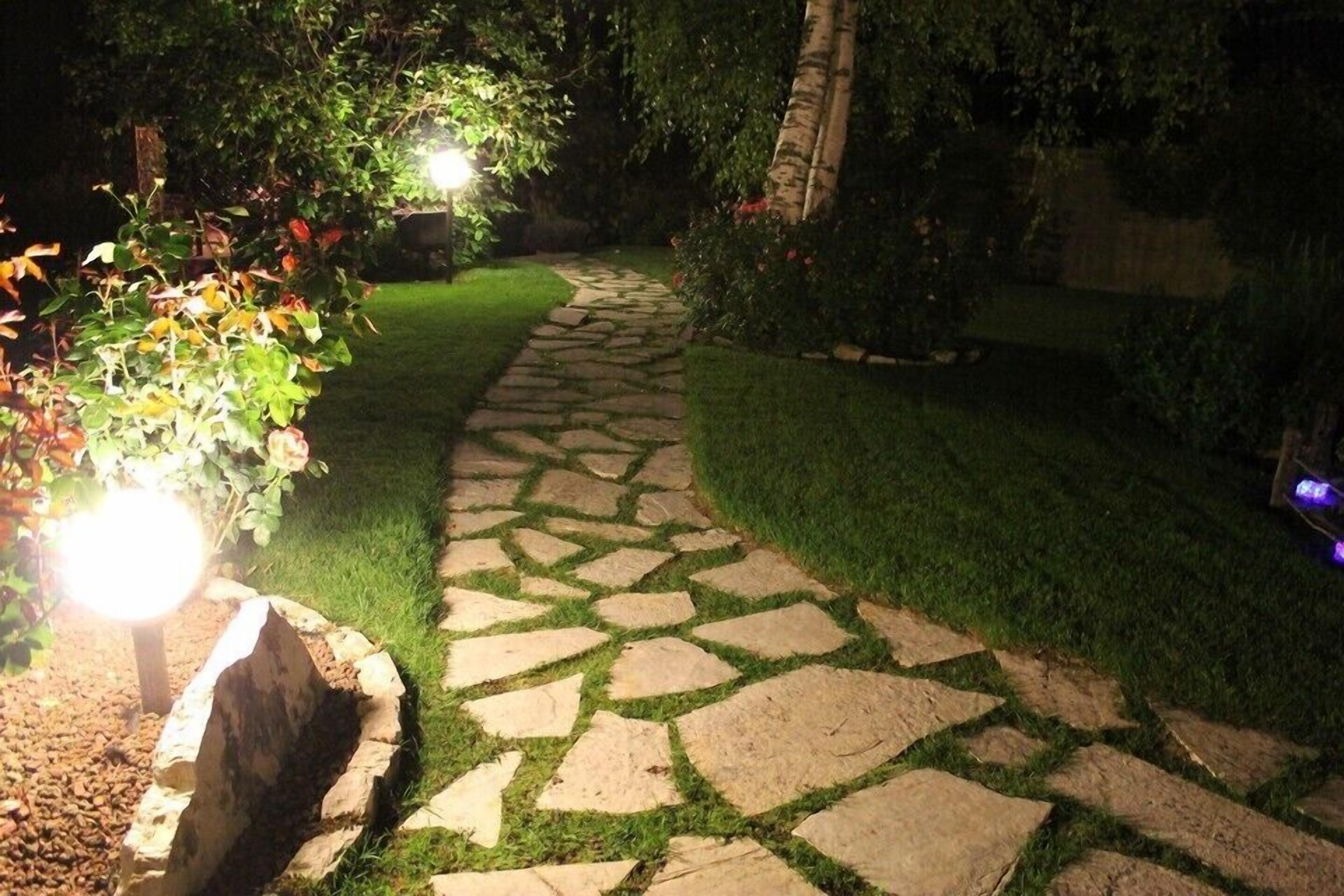 Un vialetto in pietra che si snoda in un giardino illuminato da luci da esterno.