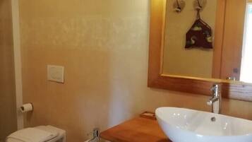 A bathroom with a wooden vanity, a white sink, a bidet, and a mirror with a floral design.