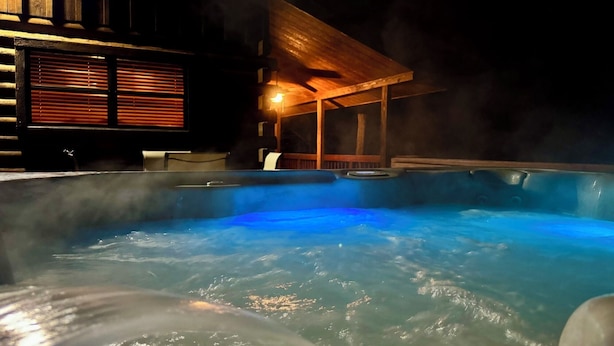 A hot tub with steam rising from the water, surrounded by a wooden deck and a covered seating area.