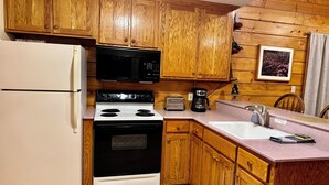 A kitchen with wooden cabinets, a white refrigerator, a black microwave, a stove, a toaster, and a coffee maker.
