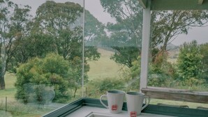 Una ventana con vistas a un paisaje verde, un libro y dos tazas en el alféizar.