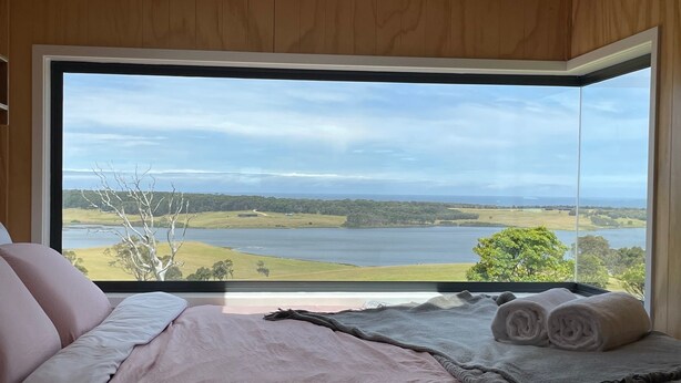 Un dormitorio con un amplio ventanal que ofrece vistas a un lago y al paisaje circundante.