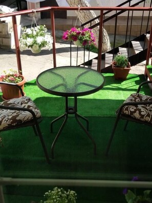 A small outdoor seating area with a round table and two patterned chairs, surrounded by potted plants and a staircase.