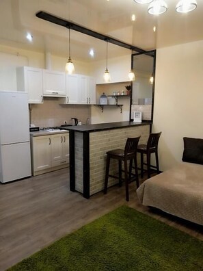 A compact kitchen with white cabinets, a black countertop, and a small dining area with two chairs.