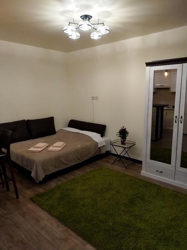 A bedroom with a bed, a small side table, a green rug, and a wardrobe.