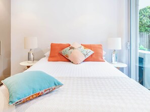 A hotel room with a large bed, two bedside tables with lamps, and a view of greenery through the window.