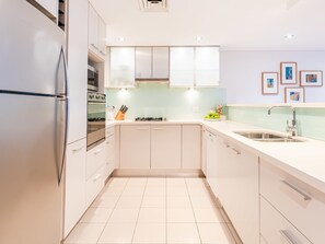A modern kitchen with white cabinets, a stainless steel refrigerator, a gas stove, and a sink.