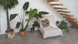 A modern living room with a sofa, a large potted plant, a hanging wooden shelf, and a staircase. - Villa of archi 180m2 new (Saint-Aunès)