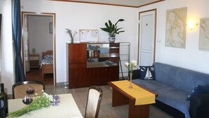 Un salon avec un canapé, une table à manger ornée d’un vase de fleurs, une bibliothèque et une plante en pot.
