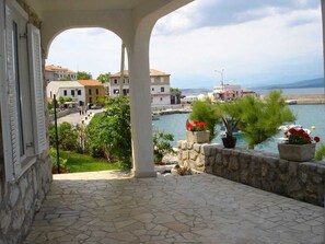 A stone-paved balcony with a view of a harbor, buildings, and a clear sky. - Apartment Jelenovic C. D. (Silo - island Krk)