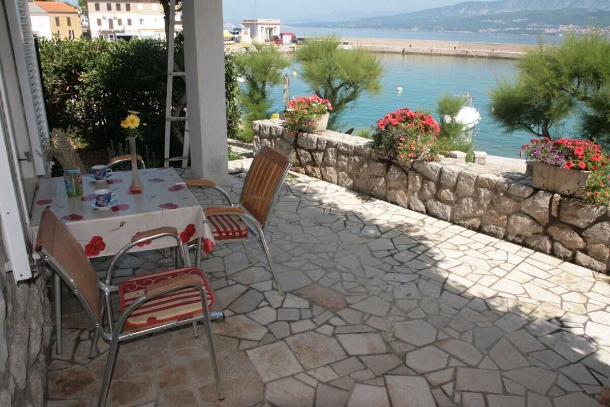 An outdoor patio with stone flooring, a table with chairs, and a view of the sea.