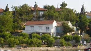 Un bâtiment situé sur la côte, doté d’un balcon, entouré de verdure et bordé par un plan d’eau.