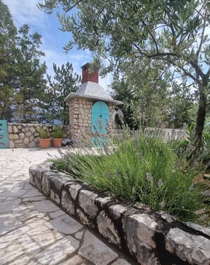 Un edificio de piedra con una puerta turquesa, rodeado de follaje y un sendero de piedra.