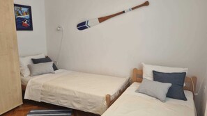A small, simple room with two single beds, a wooden paddle on the wall, and a painting. - Apartment Sanjug (Silo - island Krk)